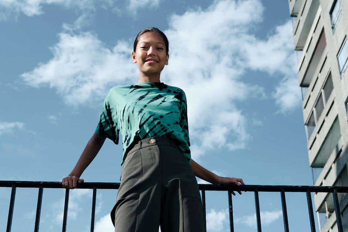an upward shot of a young smiling female leaning against a metal railing. Above her the sky is blue