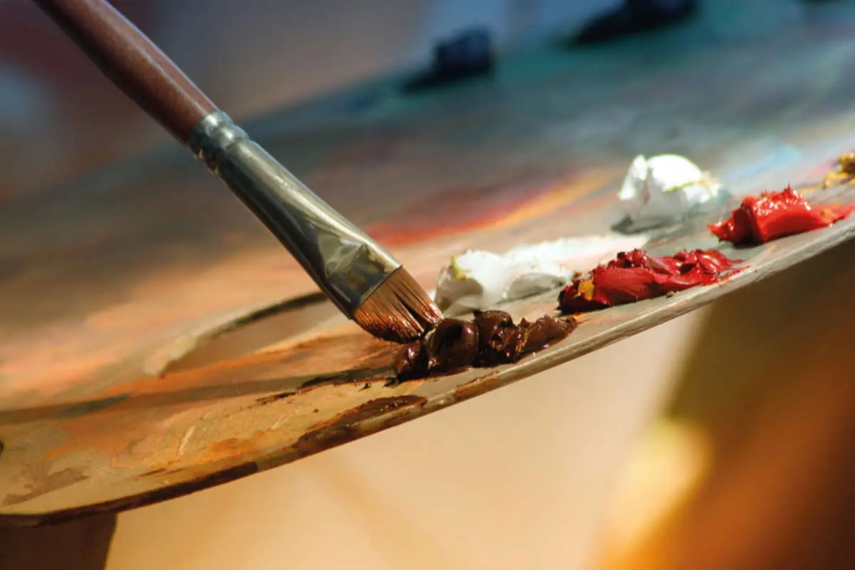 a paintbrush dipping in paint on an artists mixing palette