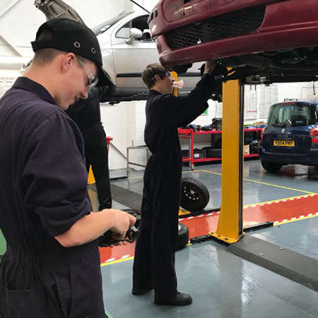 Student mechanics working on an elevated car