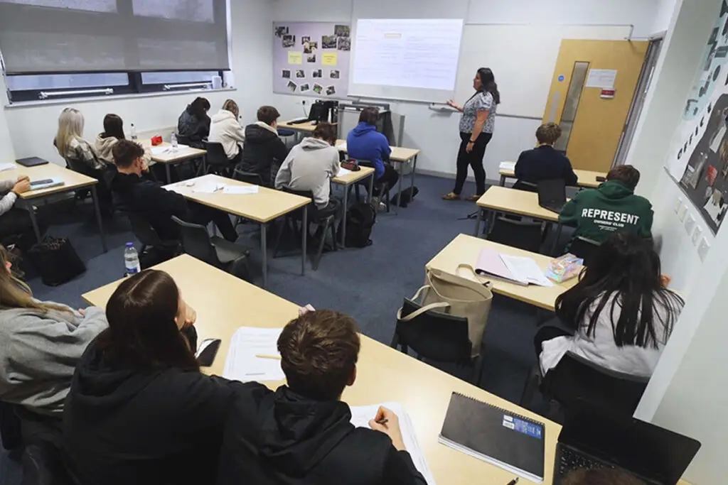 A classroom full of students. A tutor is giving standing, giving the lesson at the front of the class