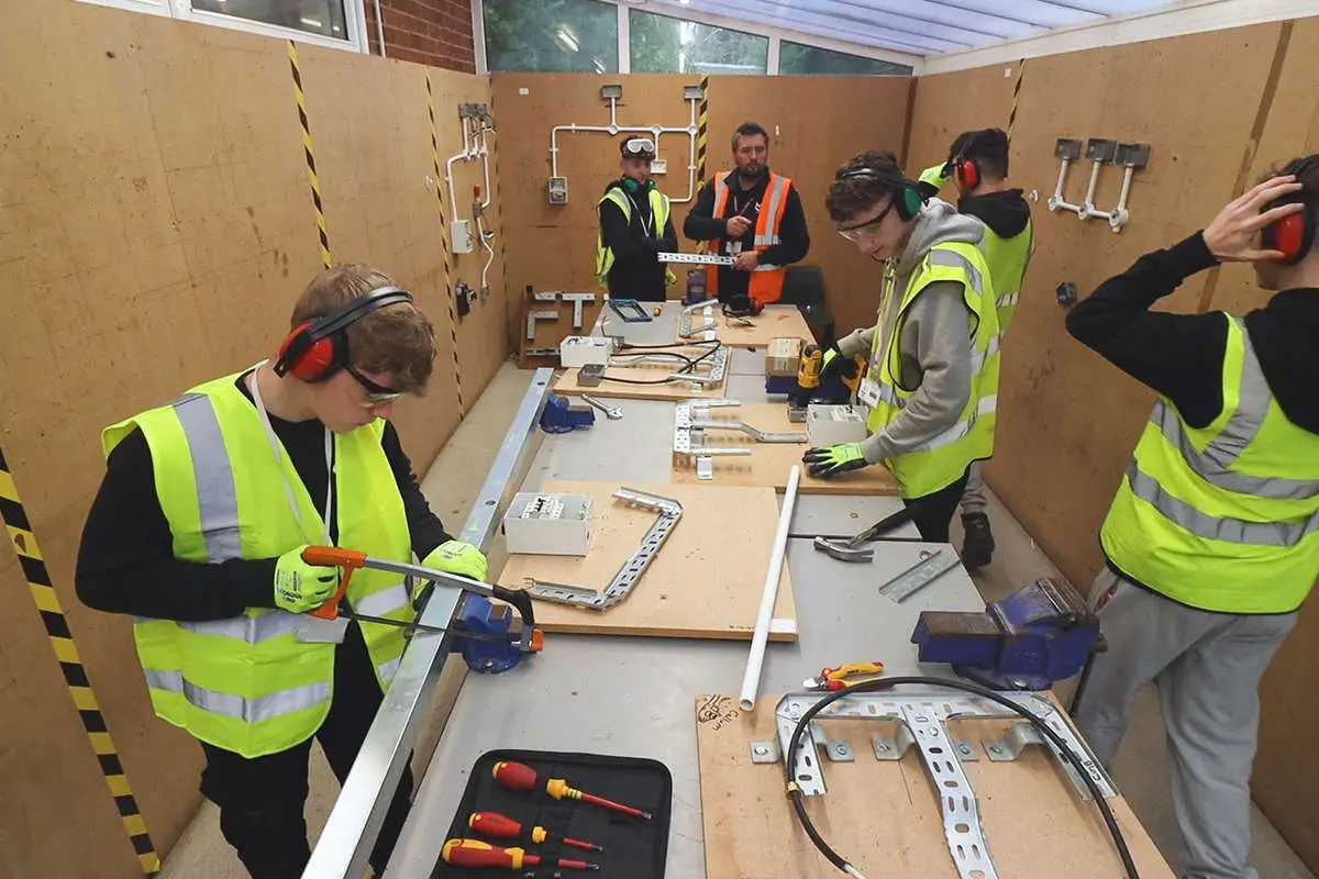 a group of students in PPE doing various constructing jobs, including sawing and drilling