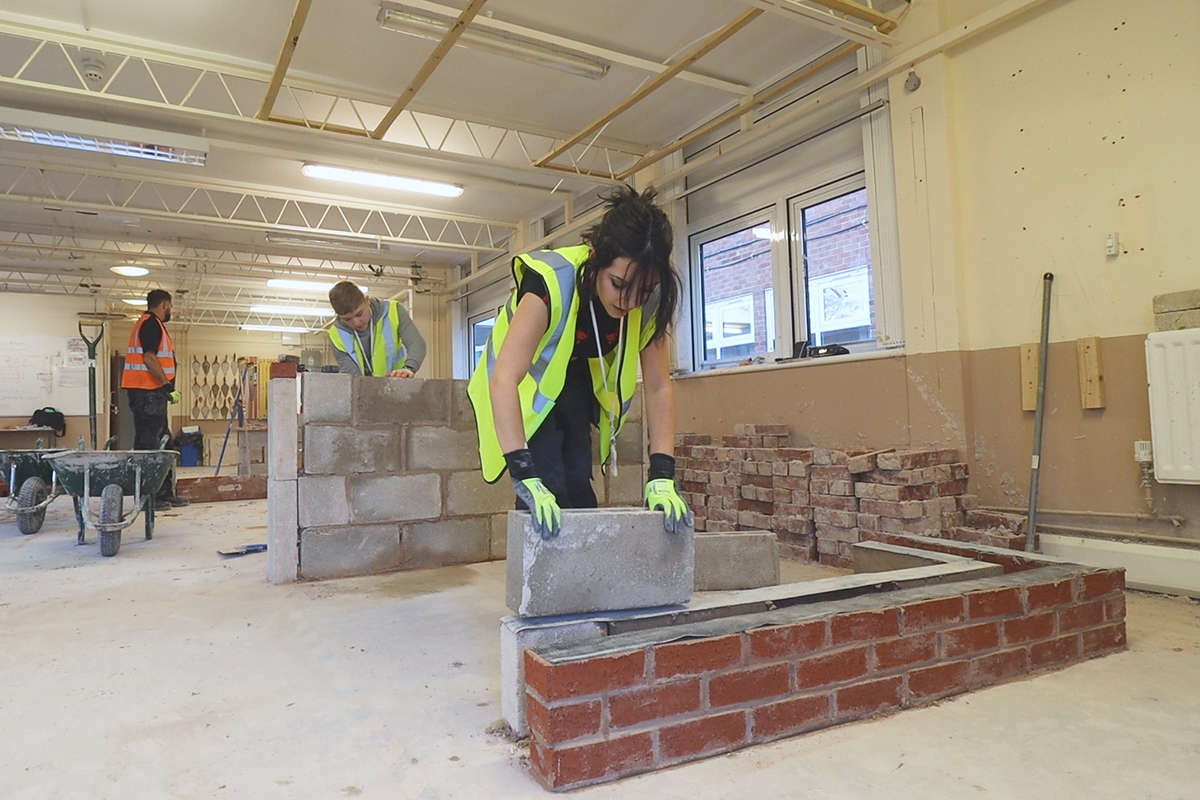 a female student wearing a hi-vis vest practices bricklaying