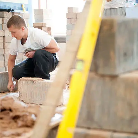 A student bricklayer crouched down surrounded by piles of bricks