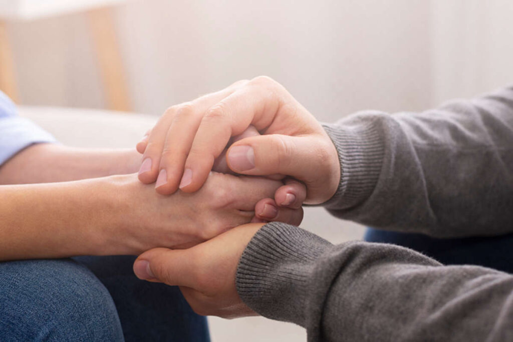A close up shot of two people holding hands in a supportive manner