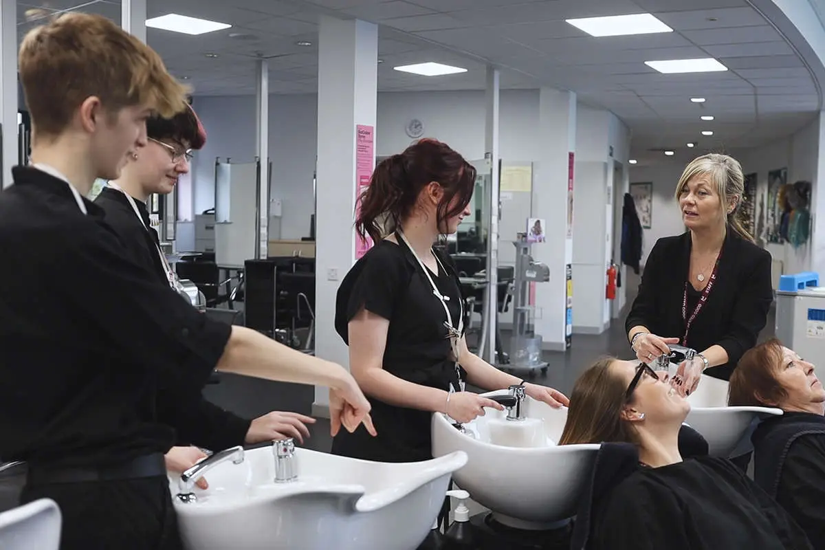 Students with a tutor, learning how to wash the hair of 2 female customers