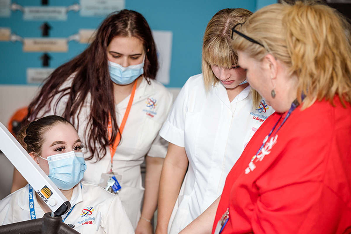 Healthcare students wearing white uniforms talk to a health worker in a red uniform