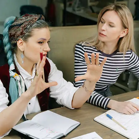 Two women having an in depth conversation with work books in front of them