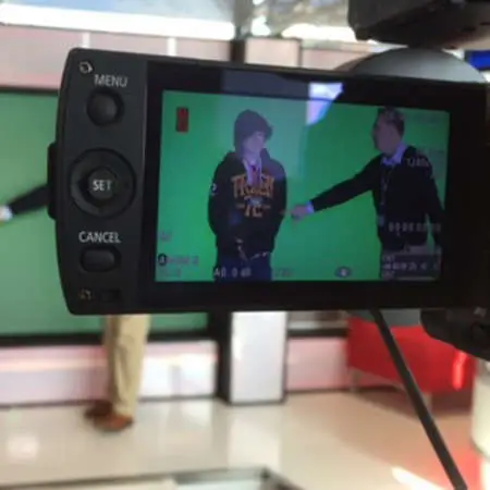 A view through a camera lens of someone in a hoody in front of a green screen