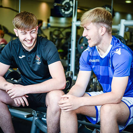 2 young males sit happily chatting in a gym