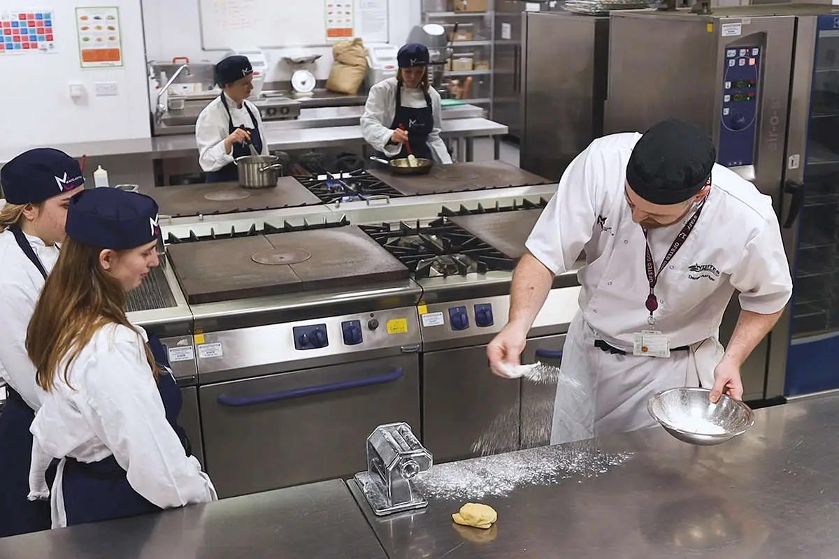 chef tutor gently dusting the counter with flour in front of several students