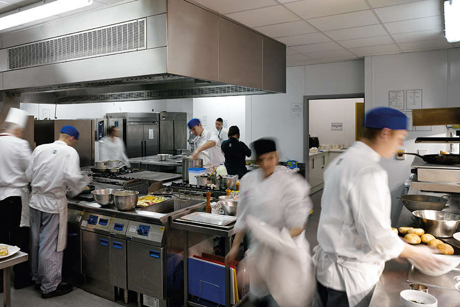 A busy working kitchen, the figures are blurred as they are hurrying about the kitchen