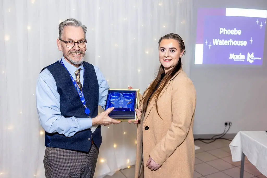 A male staff member and female apprentice are holding an award, smiling for a photo