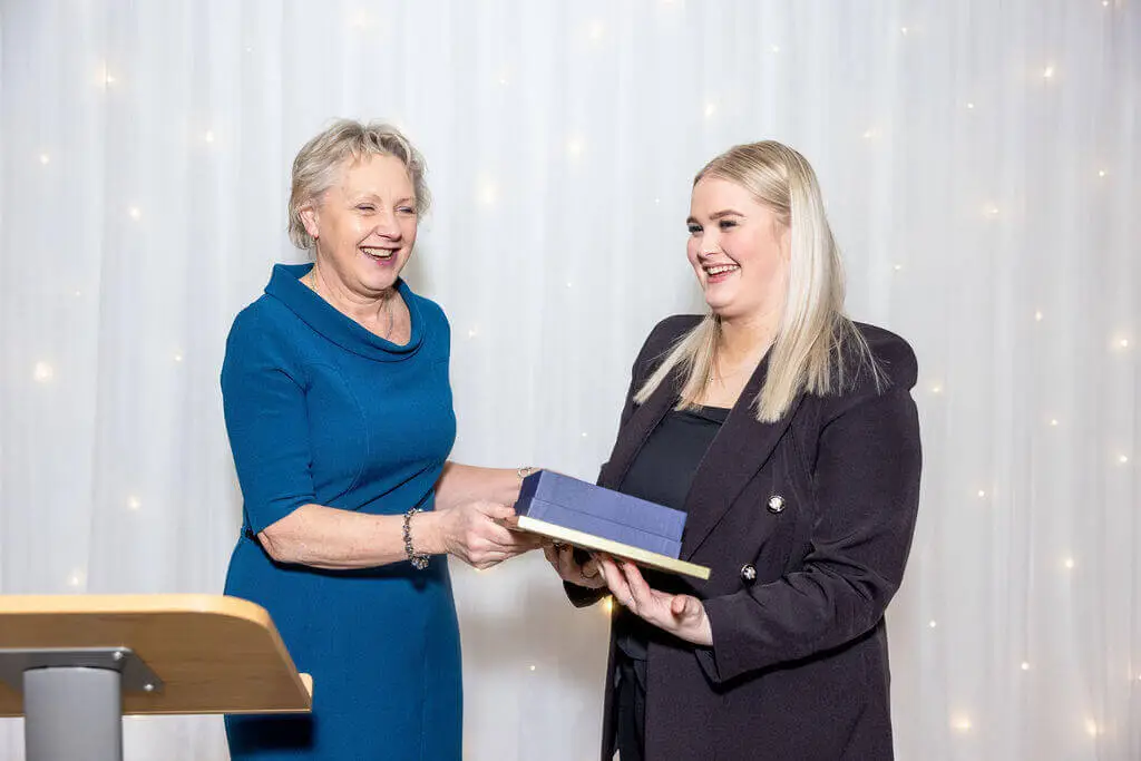 A female staff member and female apprentice are holding an award, smiling for a photo