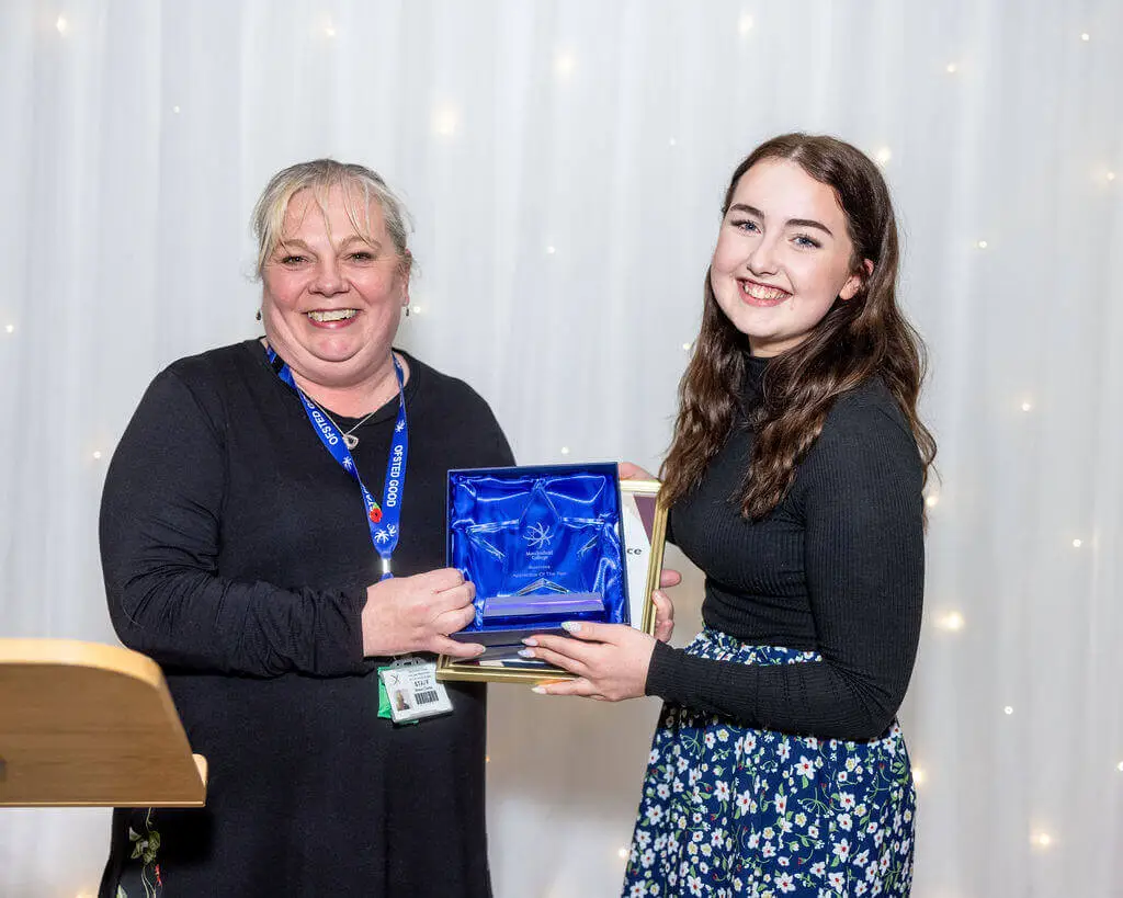 A female staff member and female apprentice are holding an award, smiling for a photo