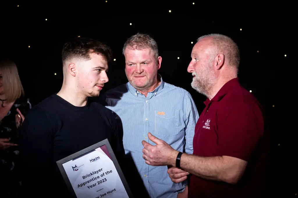 A student and two staff members are talking during an award ceremony. The student is holding a certificate