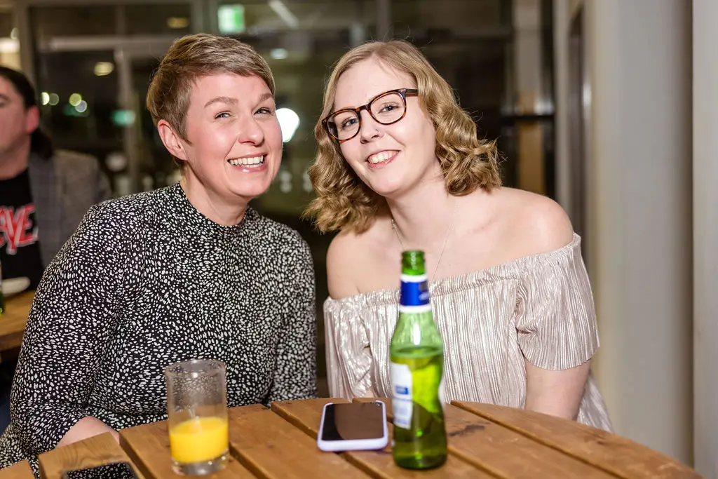 Two females are sitting at a table, smiling for a photo during an award ceremony