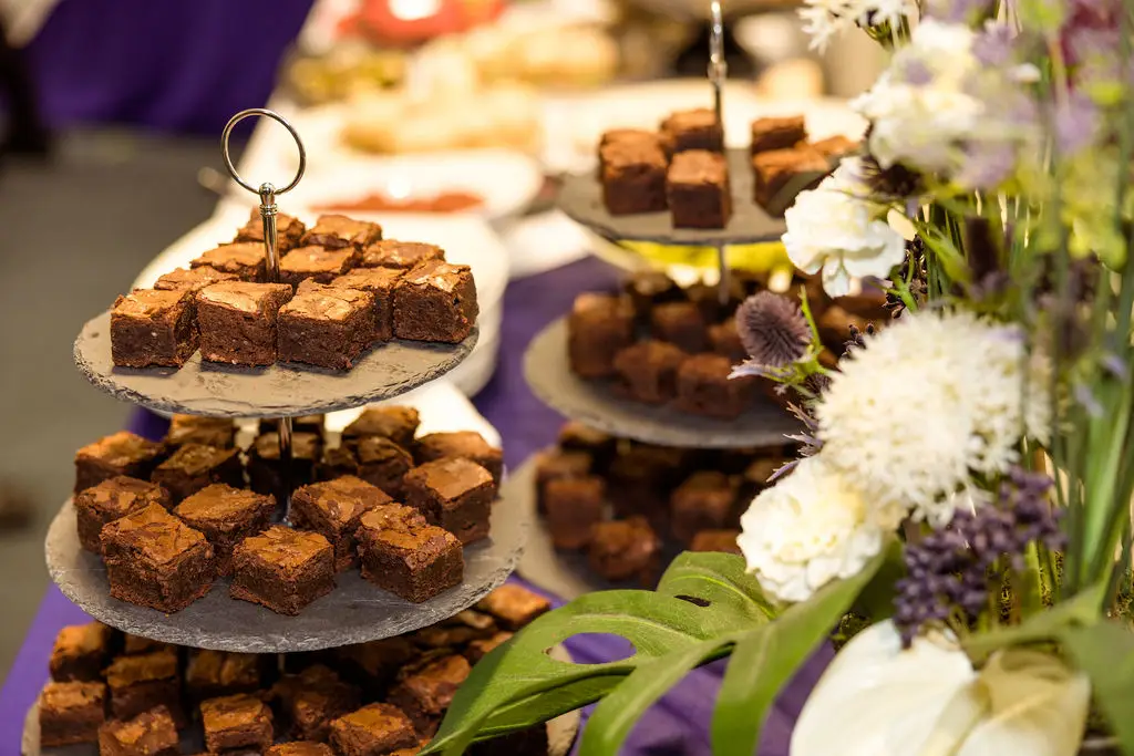 A table is decorated with a purple tablecloth and is filled with little cakes