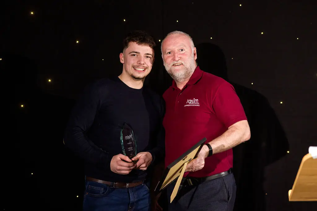 A student and a staff member are smiling for a photo during an award ceremony. The student is holding a glass award