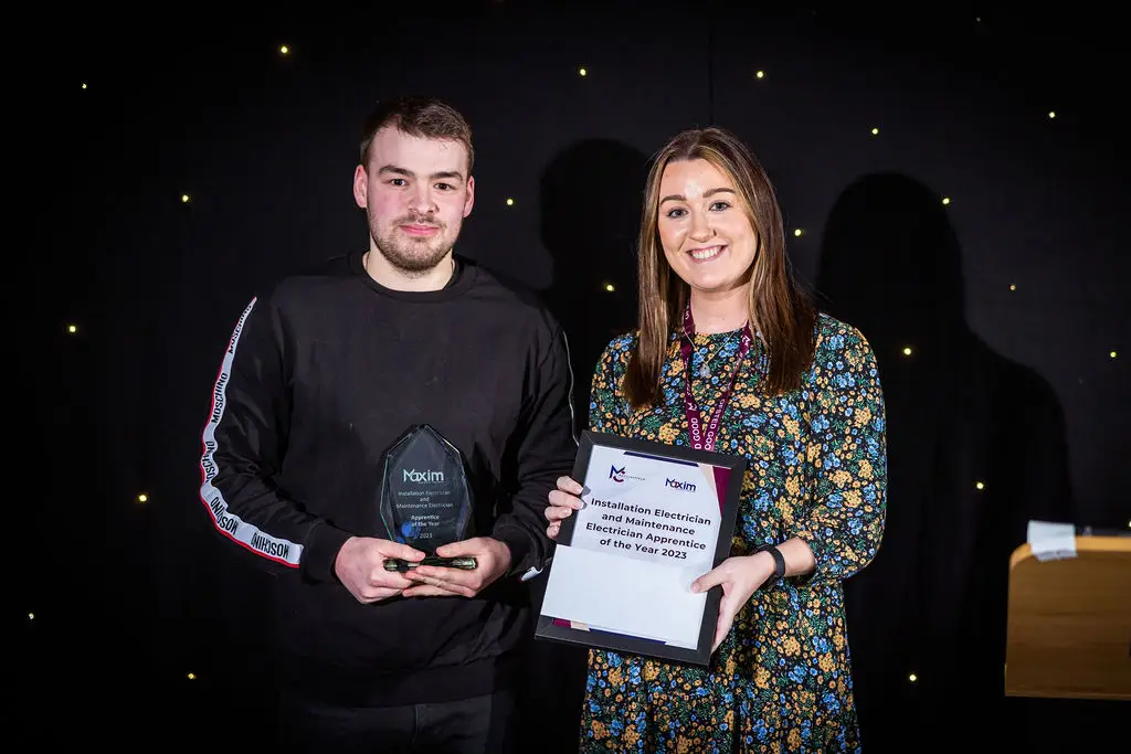 A student and a staff member are smiling for a photo during an award ceremony. The student is holding a glass award while the staff member holds a certificate