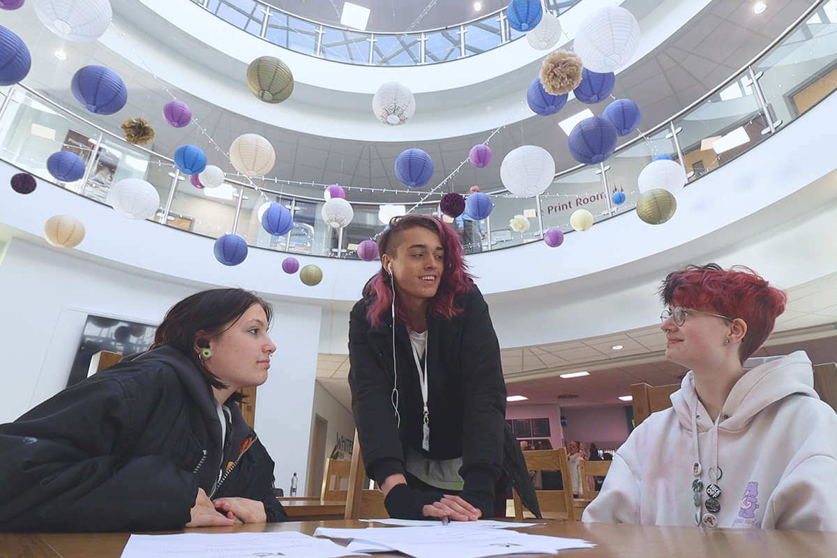 A group of students talking happily in macclesfield college foyer with the ceiling filled with balloons