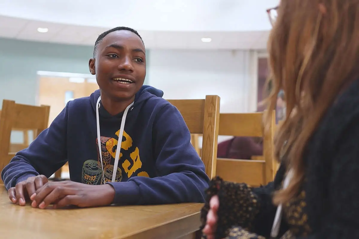 2 students in conversation, sat down at a desk