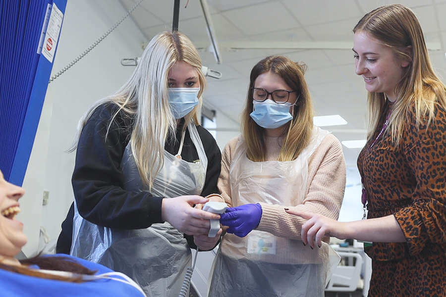 healthcare students in a mock hospital setting, adjust a patient bed