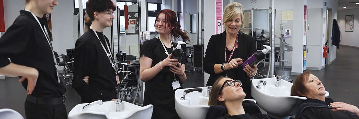 A group of beauty students and teachers talking laughing and washing customers hair