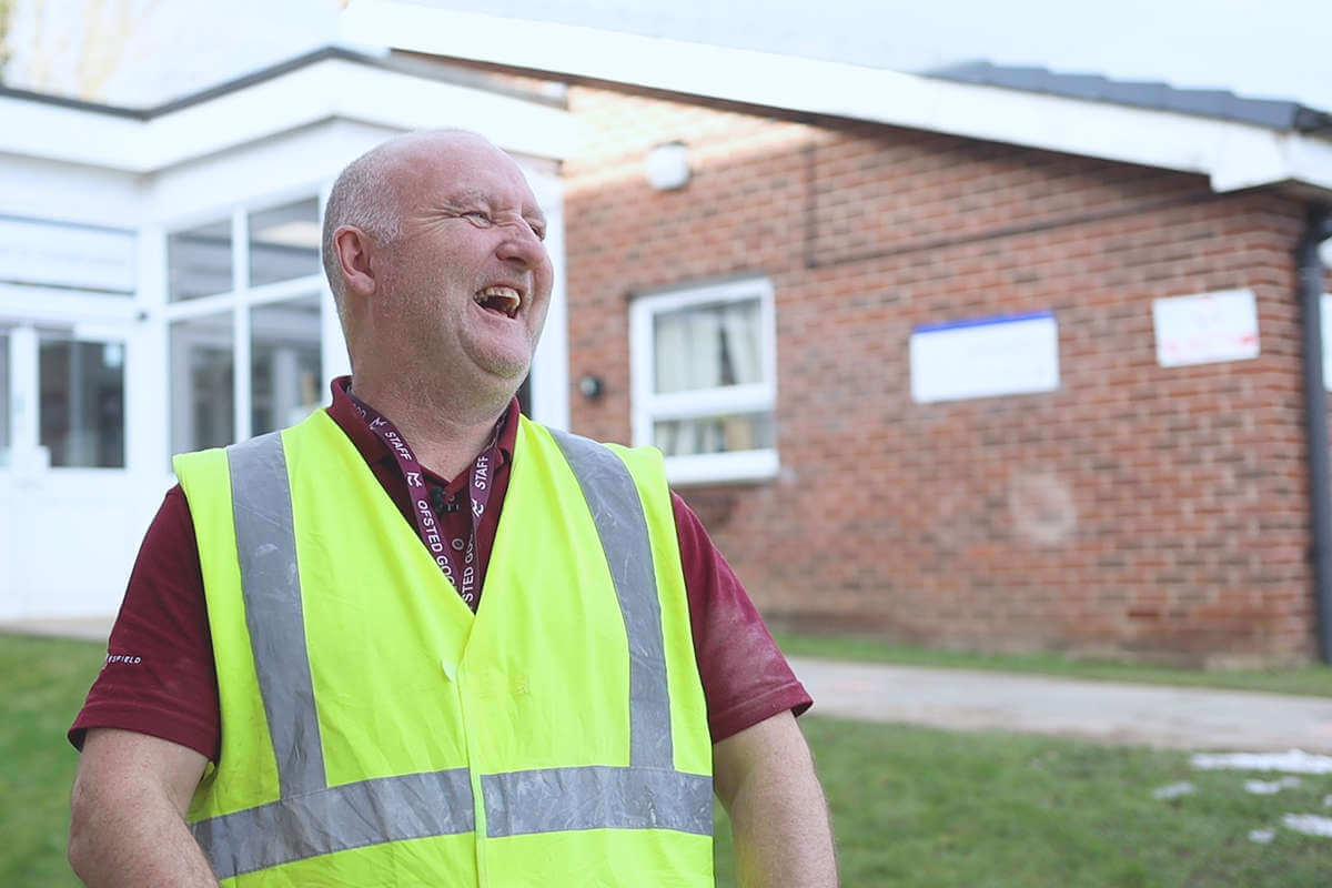 A member of staff, outside wearing a Hi-Vis vest, laughing
