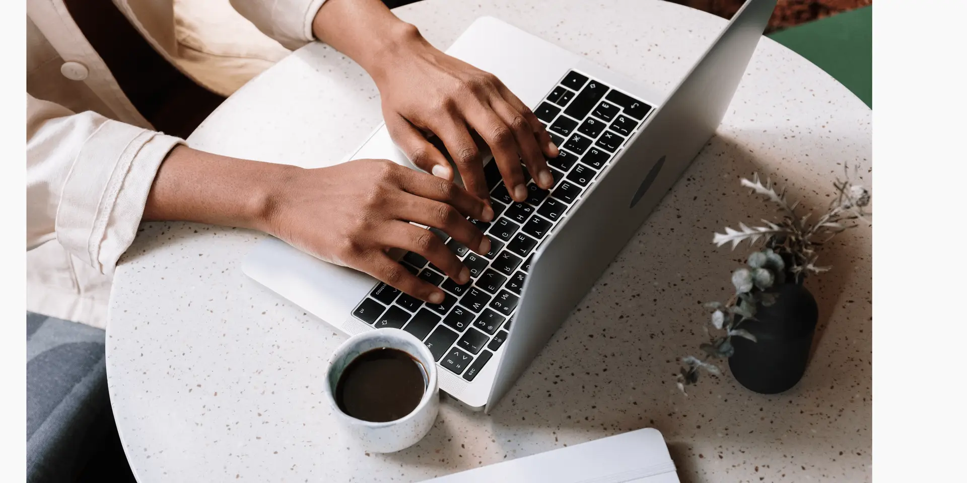 An apprentice typing on a laptop with a coffee next to them