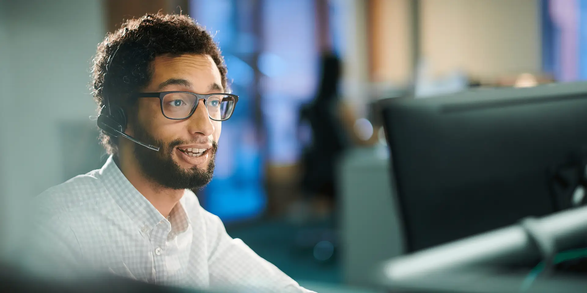 A man working in a customer services office with a head set on, talking to a customer