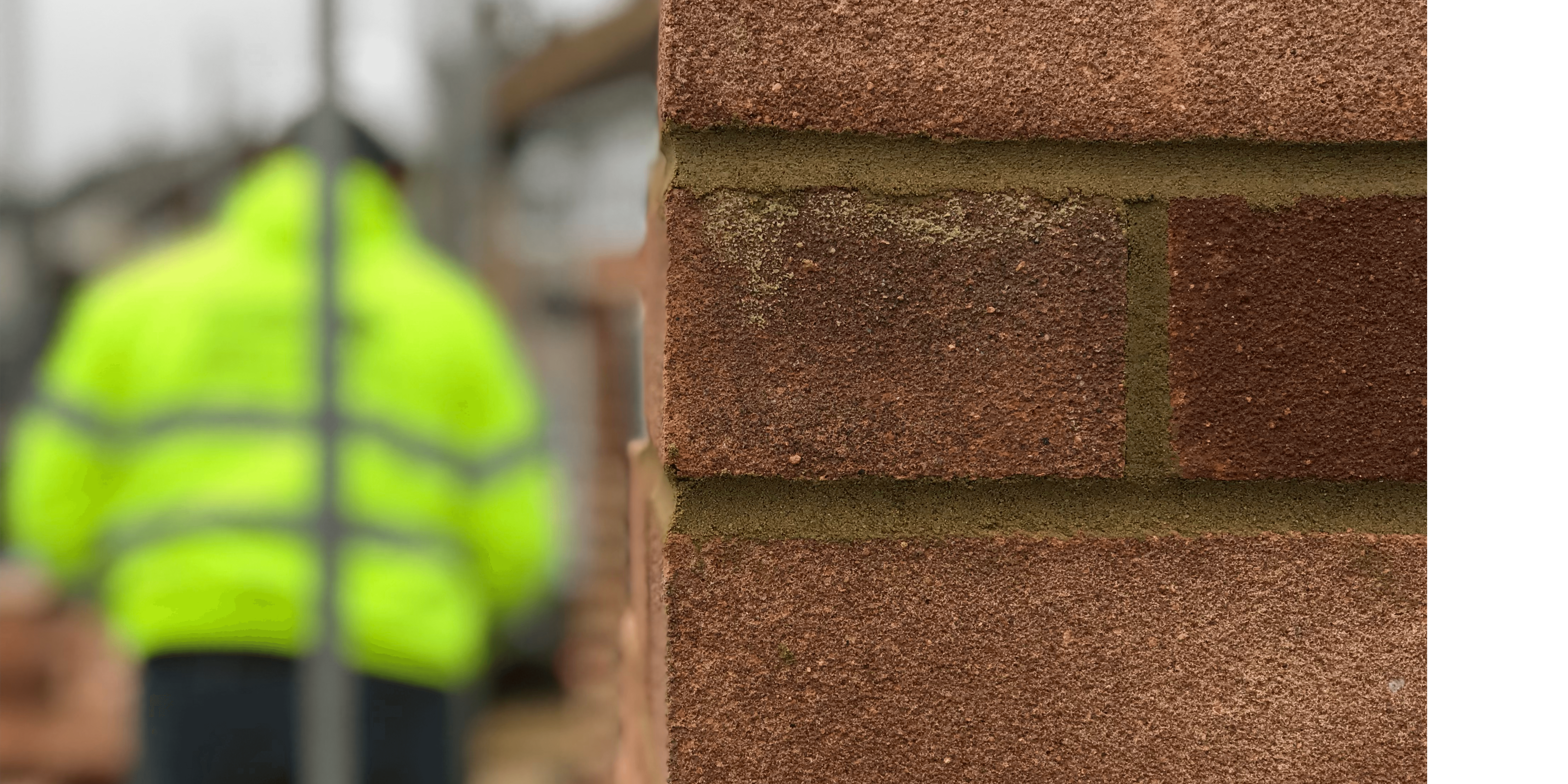 A construction site with a brick wall and a person wearing a yellow high vis jacket