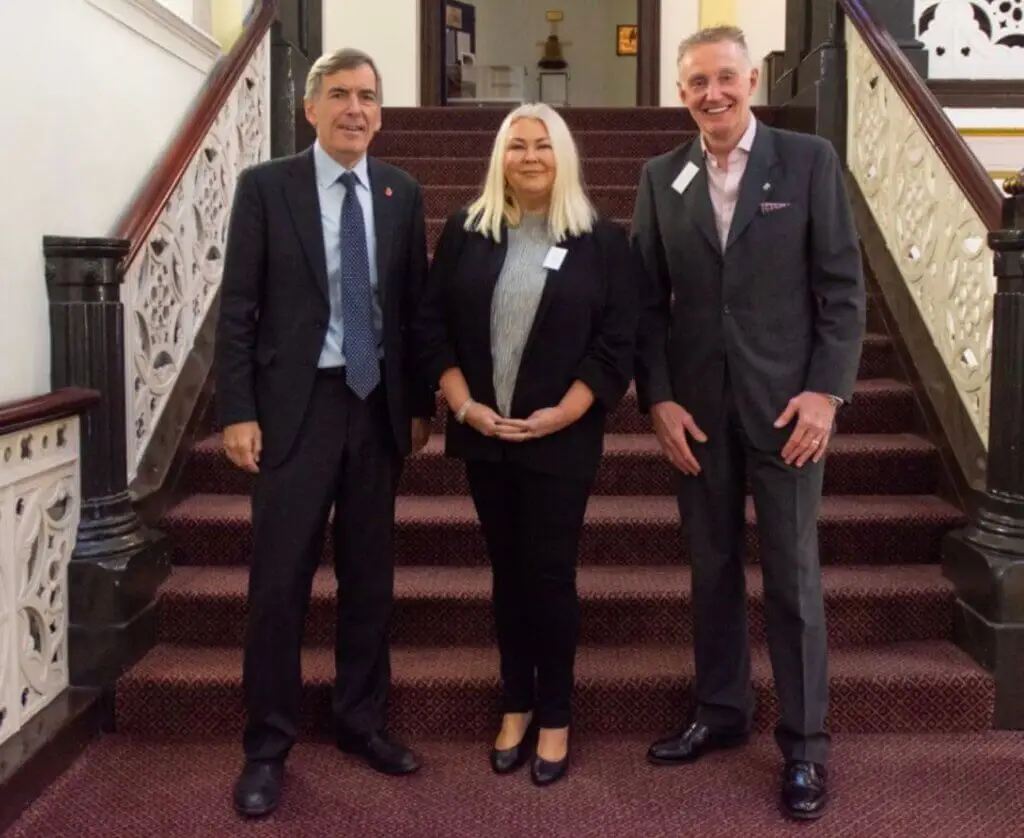Three people, dressed in business attire, are smiling for a photo