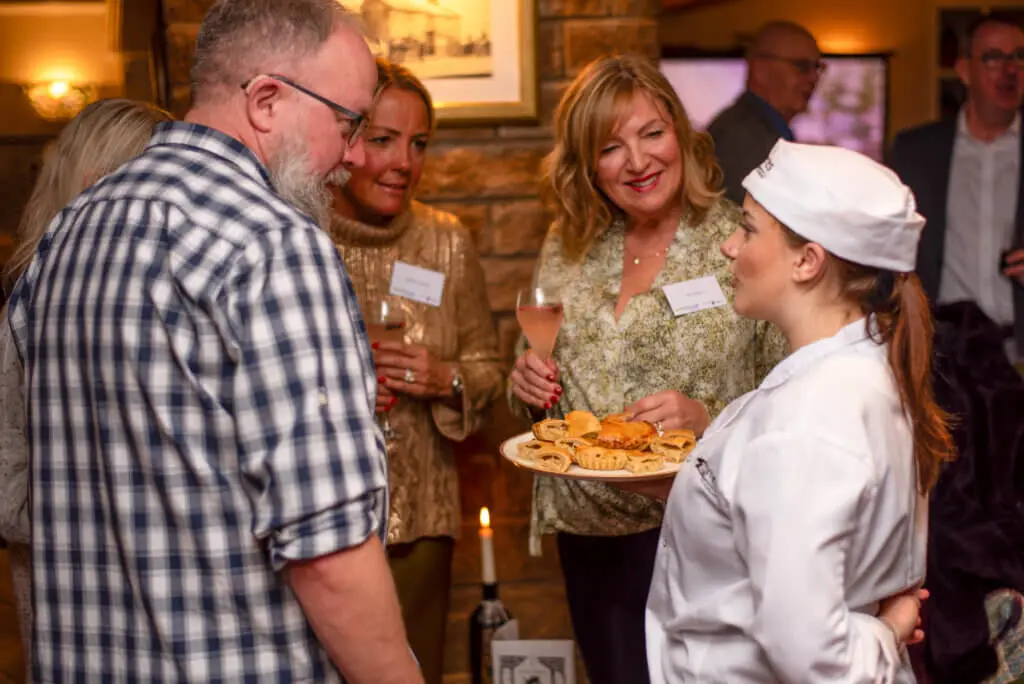 A female whites chef academy student is talking a group of people during an event