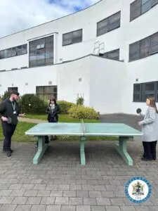 Two students playing table tennis outside while another student watches