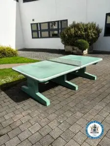 A green table tennis table set outdoors on a bright, sunny day.
