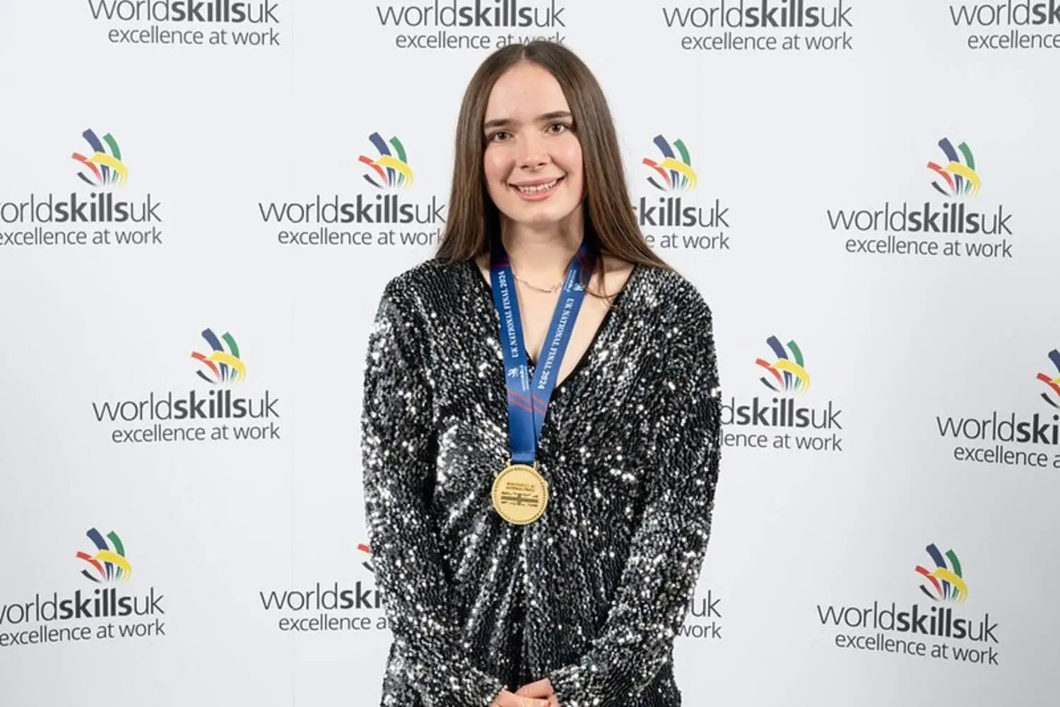 A student wearing a gold medal is smiling for a photo