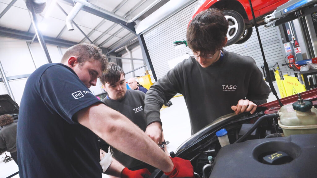 Two Automotive students and one teacher working together to look under the hood of car