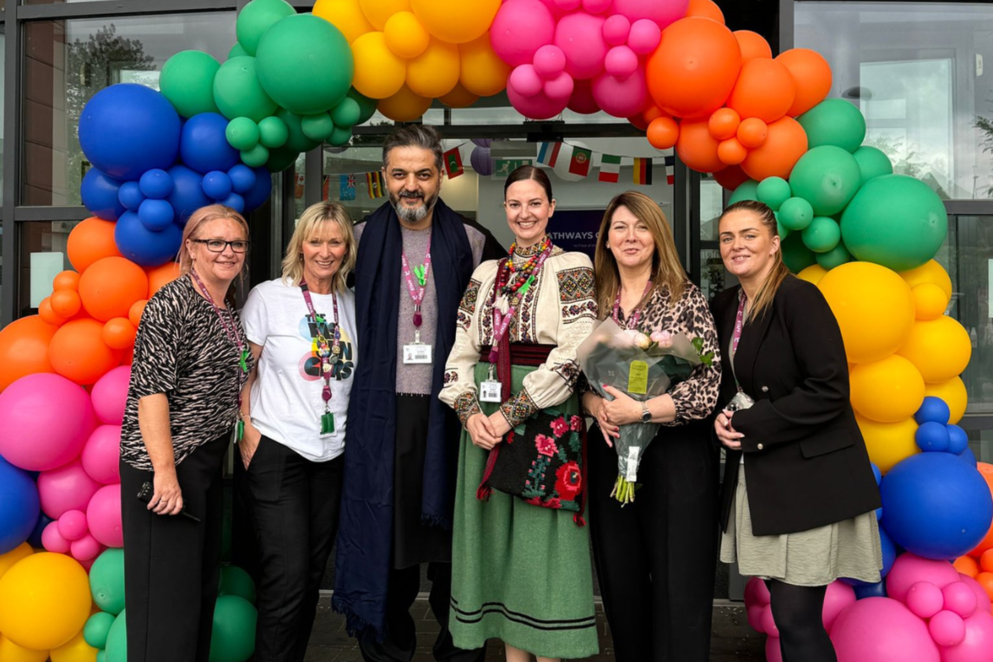A photo of Macclesfield College's EDIE team standing by a rainbow balloon arch, smiling for a photo.