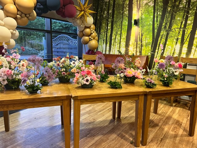 a table is neatly arranged with floristry arrangements made by adult learners from Macclesfield College