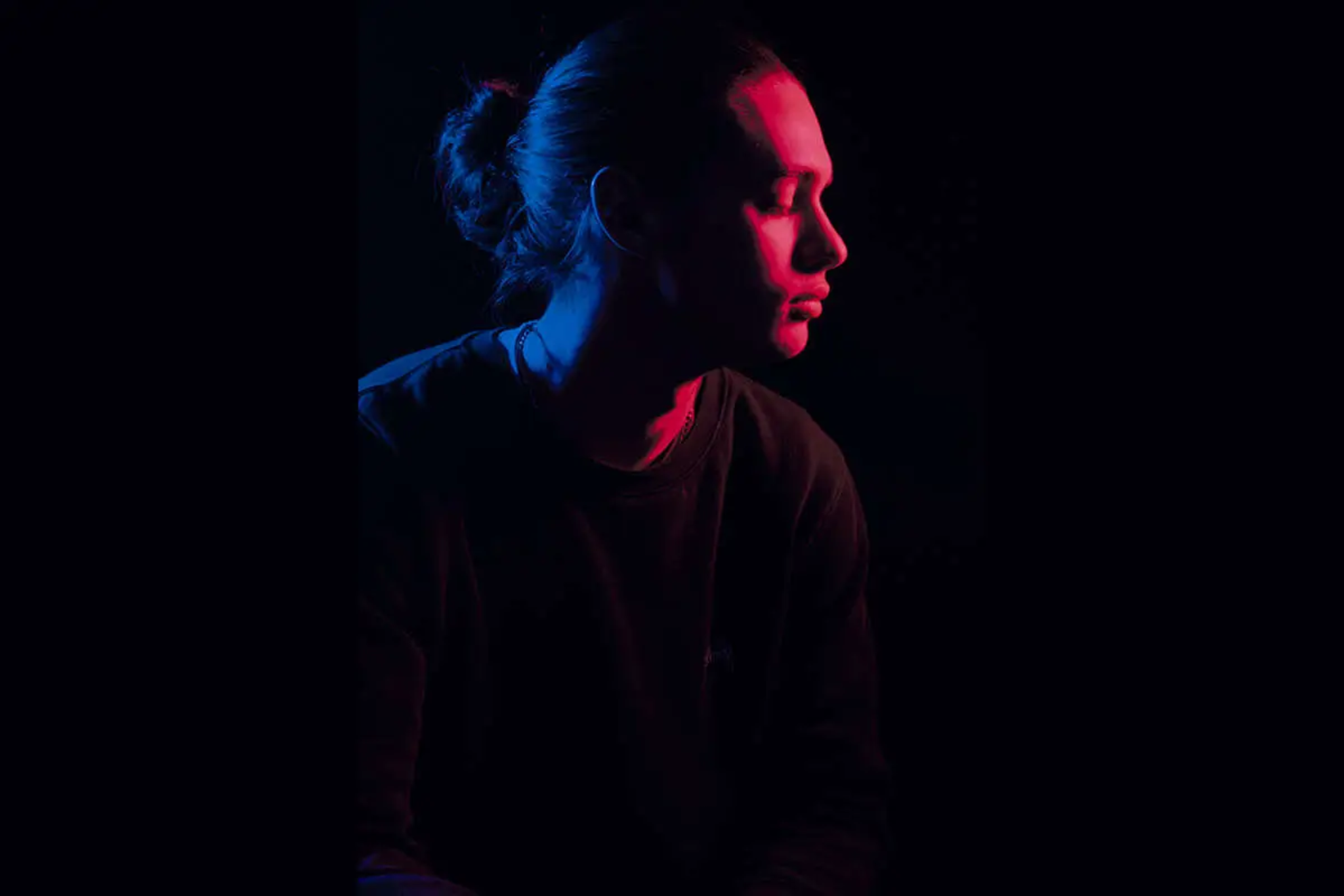 A side view of a portrait photo. On the photo a person illuminated in red and blue light