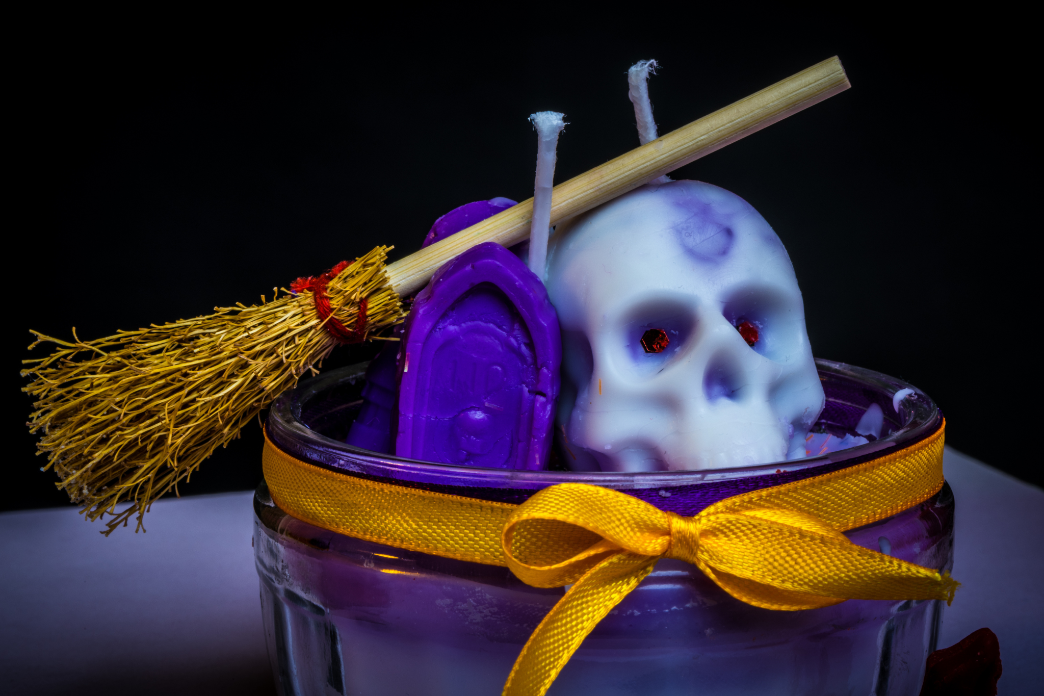 A Halloween candle containing a purple grave, a white skull and a broomstick.