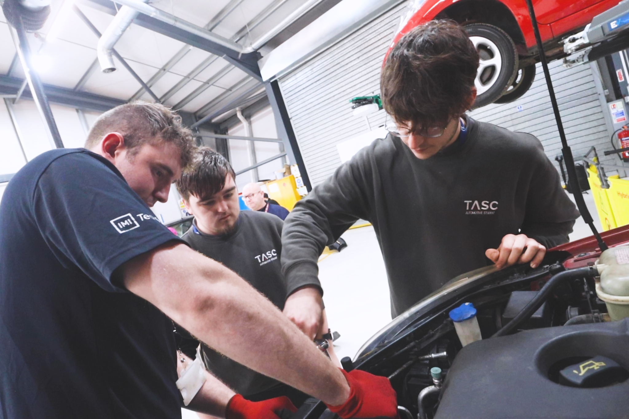 Two Automotive students and one teacher working together to look under the hood of car