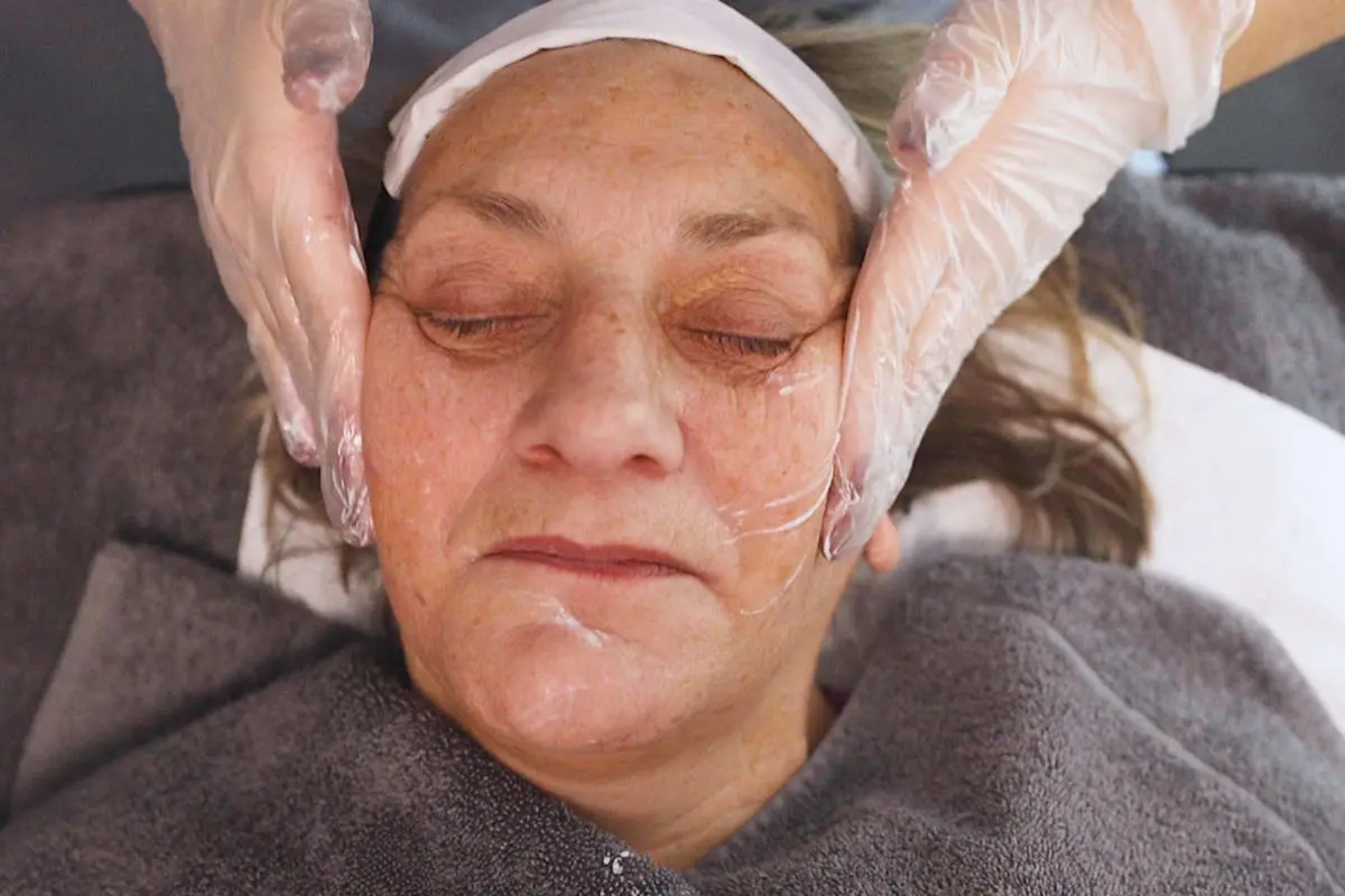 The image shows a close up shot of a woman with her eyes closed being given a facial treatment.