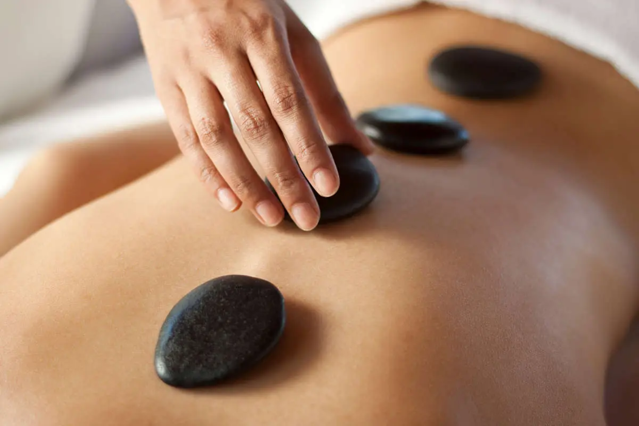A hand is placing stones onto someone's back during a beauty treatment.