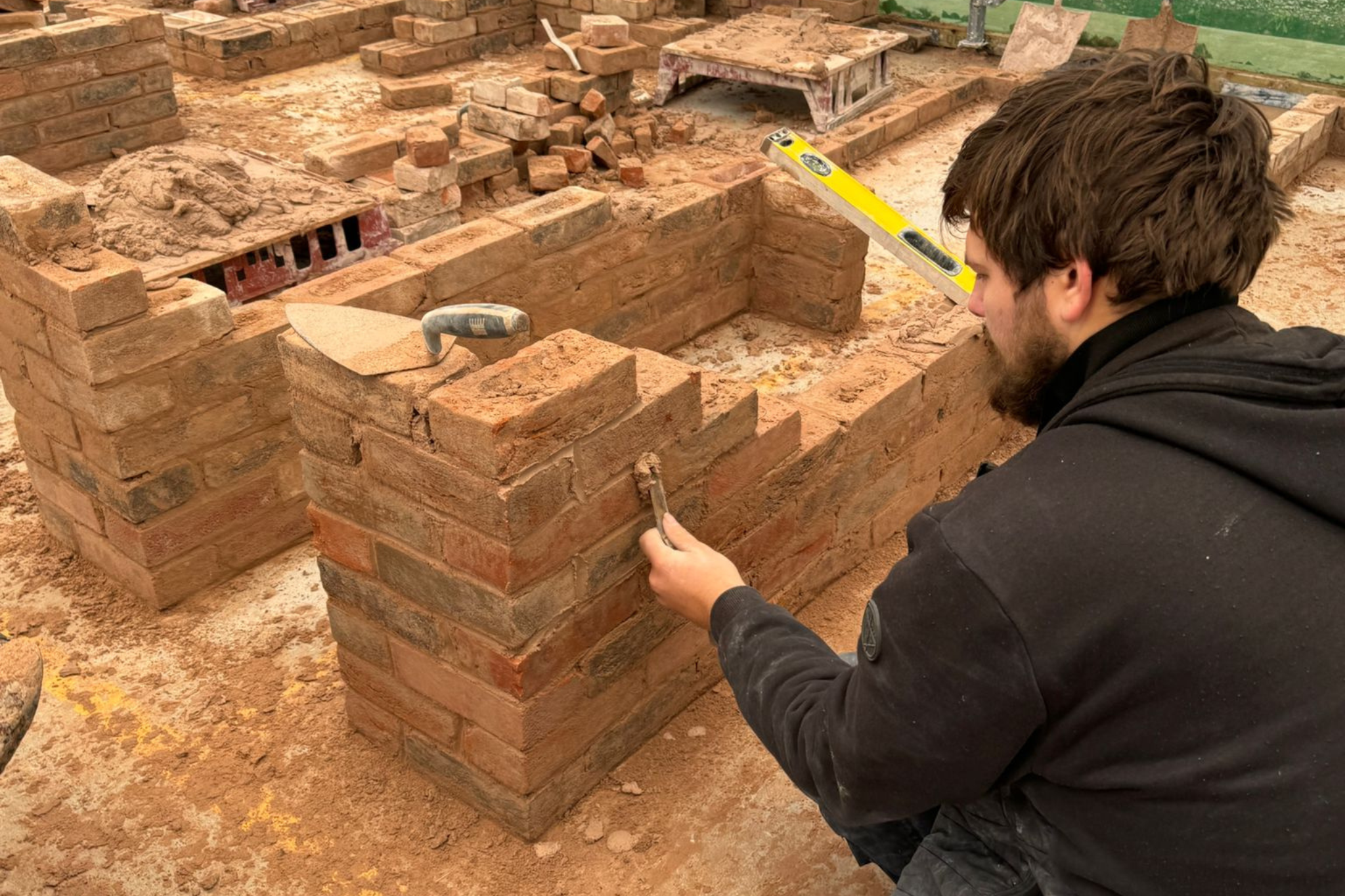 A bricklaying student is putting cement on a brick wall