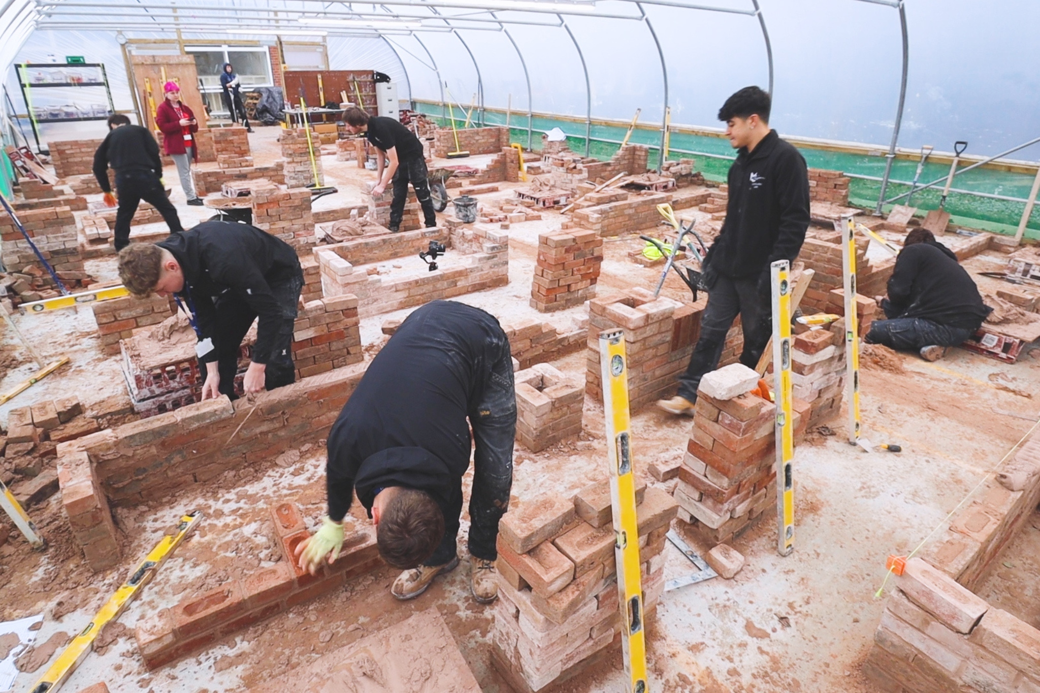 Bricklaying students are working in the workshop, building brick walls.