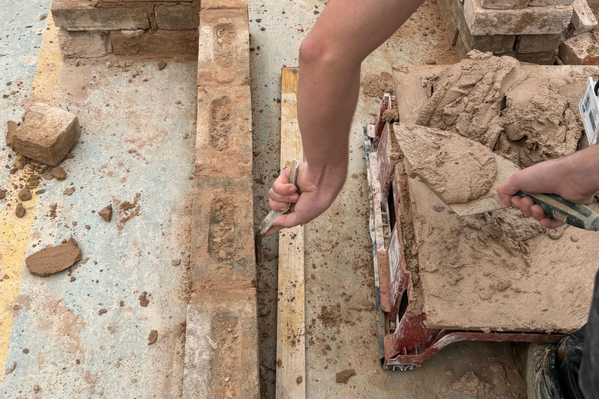A bricklaying student is putting cement on a brick wall