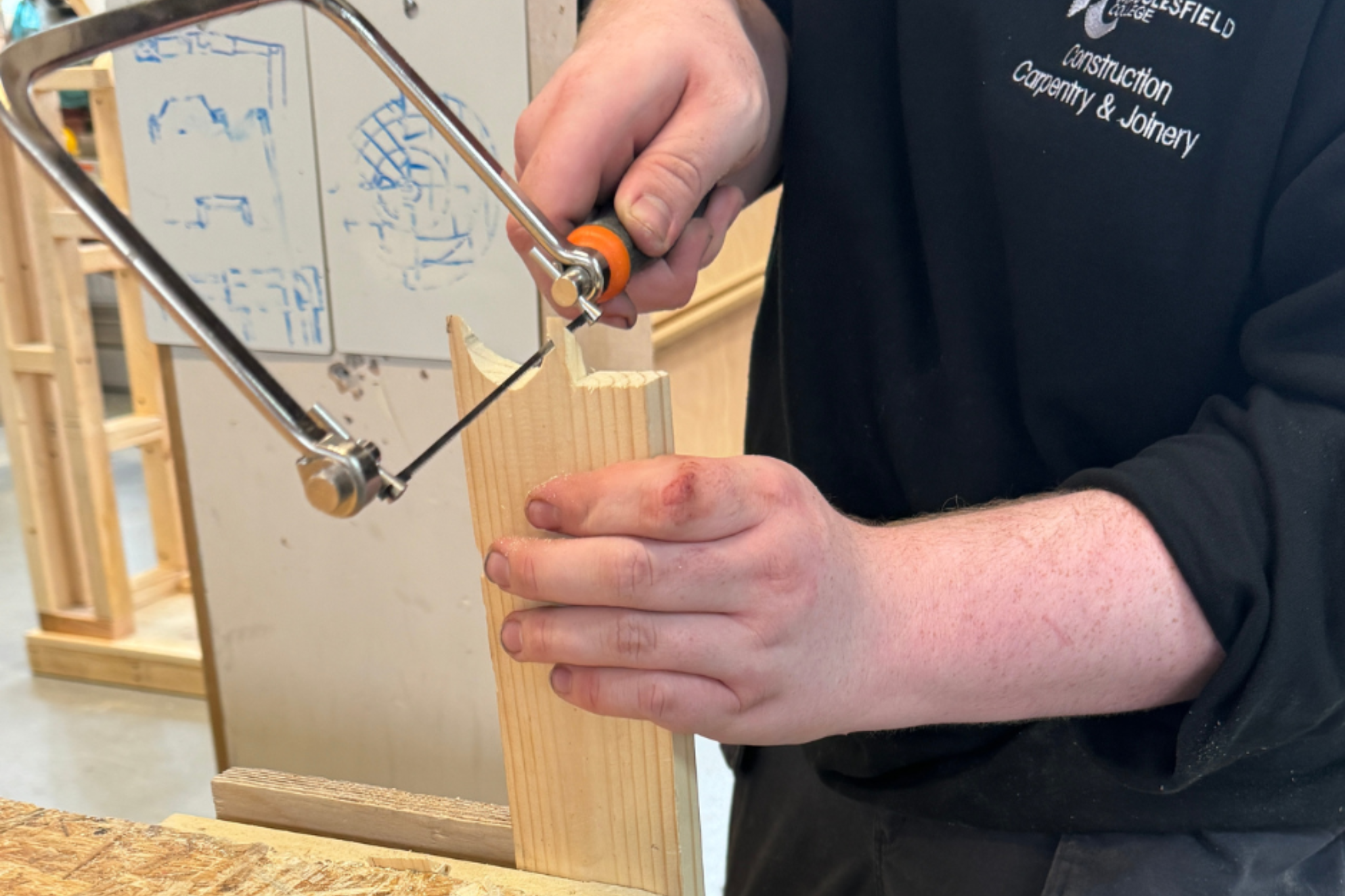 A carpentry and joinery student is using equipment to saw wood.