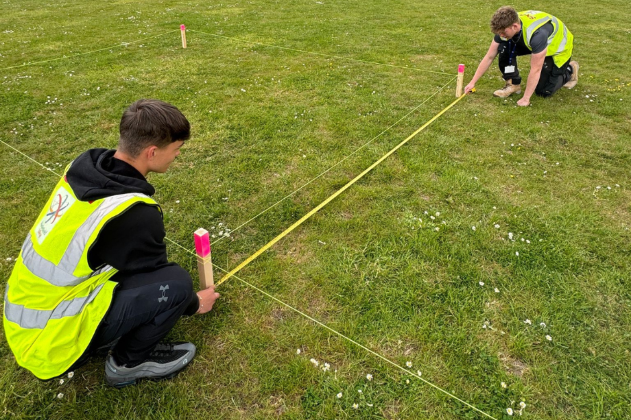 Two Carpentry and Joinery apprentices are measuring the ground to plot groundwork dimensions from drawings.