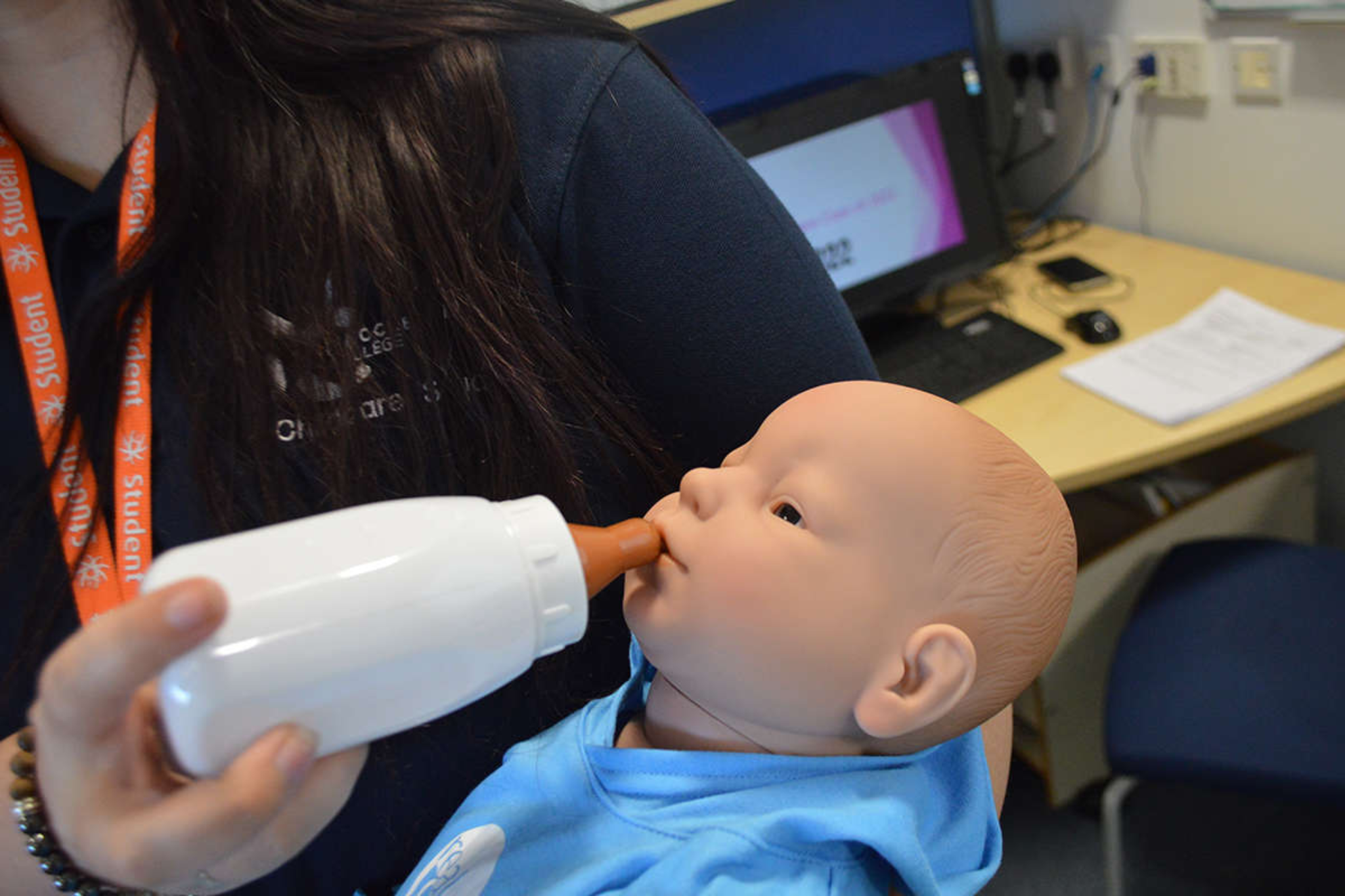 A childcare student practices giving a bottle to a baby doll